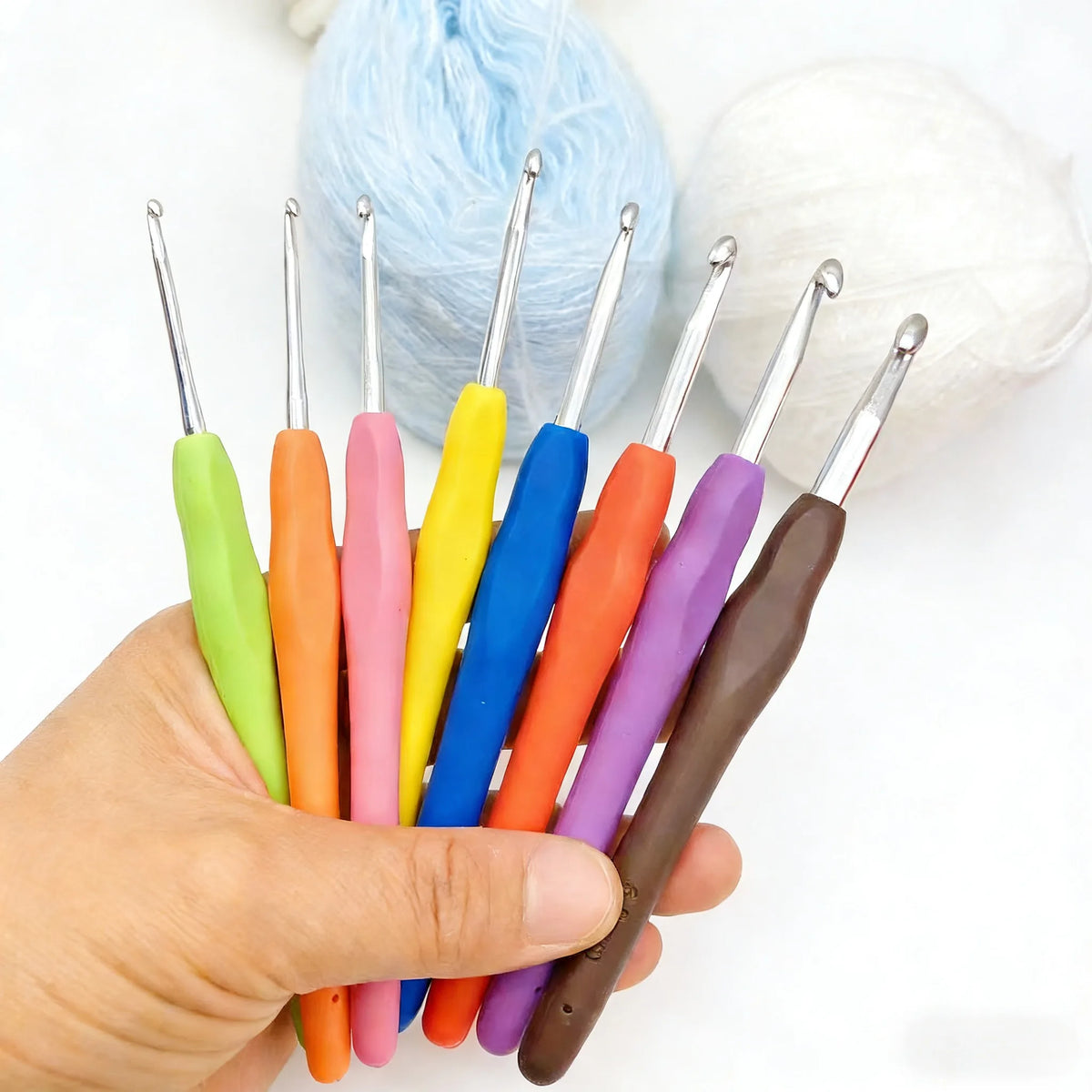 A hand holds an 8-piece crochet hook set with colorful ergonomic knitting needles in various sizes.
