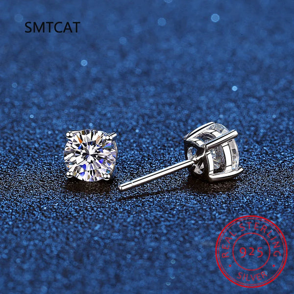 A pair of brilliant clear stud earrings made of moissanite set in 14K white gold on a dark blue surface.