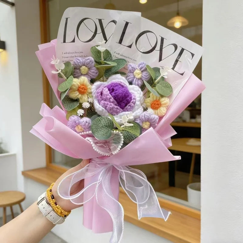 A bouquet of handmade crochet artificial flowers in purple and yellow hues wrapped in pink paper