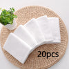 A stack of twenty white soft cotton terry cloth face towels resting on a woven mat next to a small potted plant.