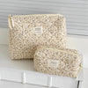 A beige floral quilted cosmetic bag with a light yellow lining resting on a white surface.