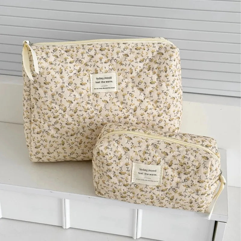 A beige floral quilted cosmetic bag with a light yellow lining resting on a white surface.