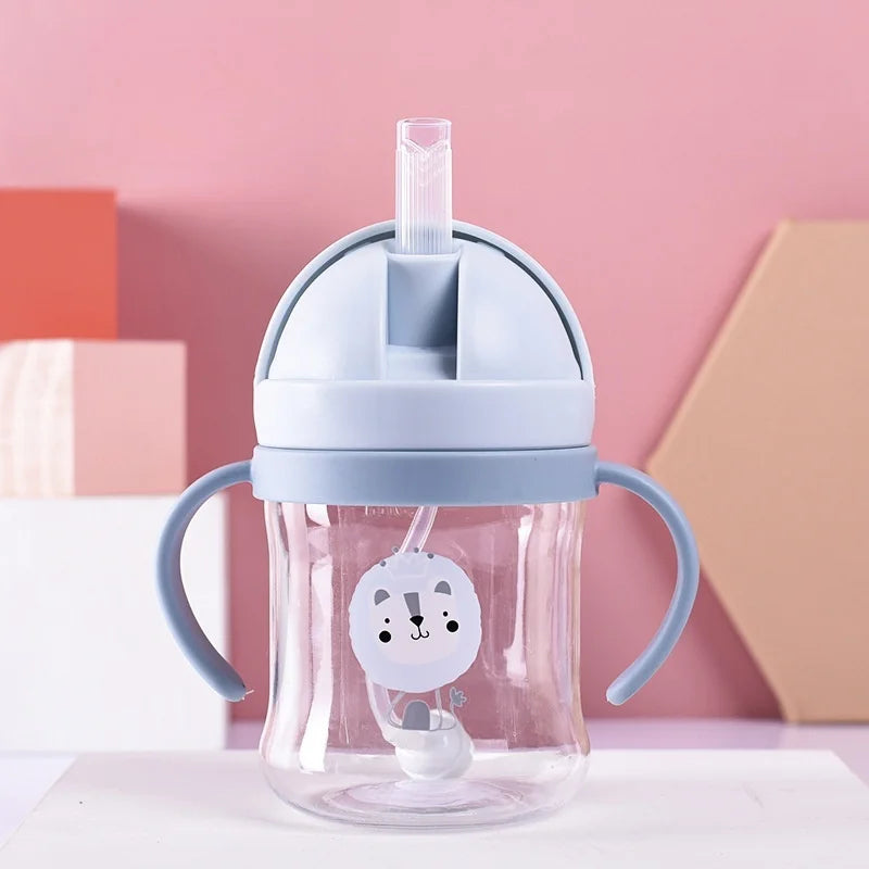 A clear glass straw cup with a silicone lid and handles in light blue and white against a pink background.