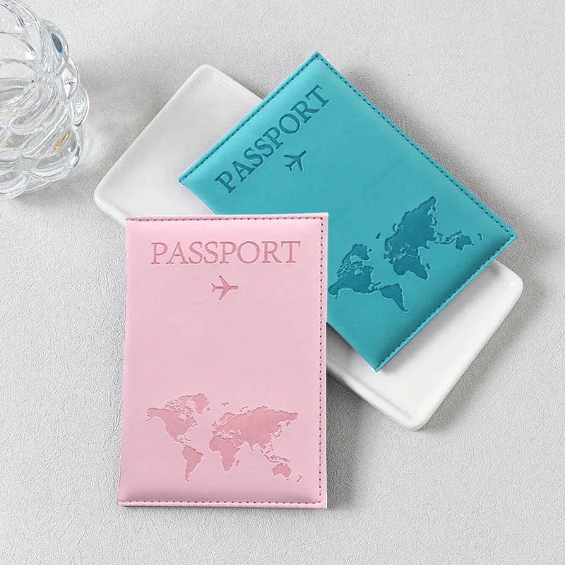 Two passport holders, one teal and one pink, featuring world maps and airplane icons, resting on a light surface.