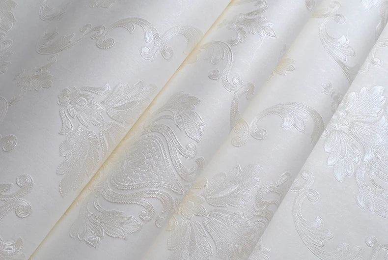 Roll of white embossed damask wallpaper featuring delicate floral scroll designs.