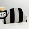 Bolso de mano tejido con rayas verticales negras y blancas, mostrado junto a una rosa y una tarjeta numerada.