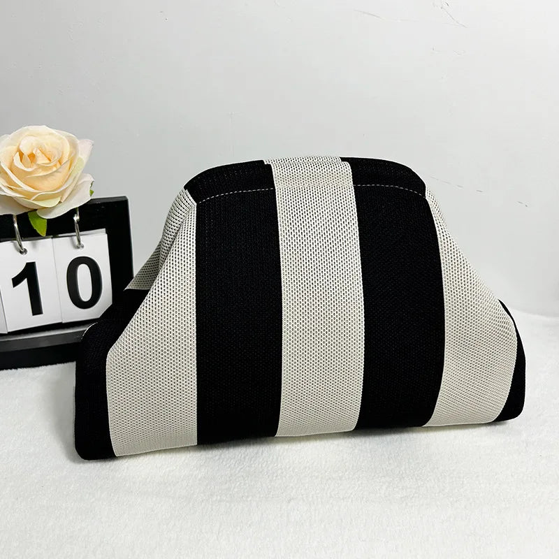 Bolso de mano tejido con rayas verticales negras y blancas, mostrado junto a una rosa y una tarjeta numerada.