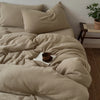 Beige, faltige Bettdecke mit passenden Kissen und Holzregal im Hintergrund.