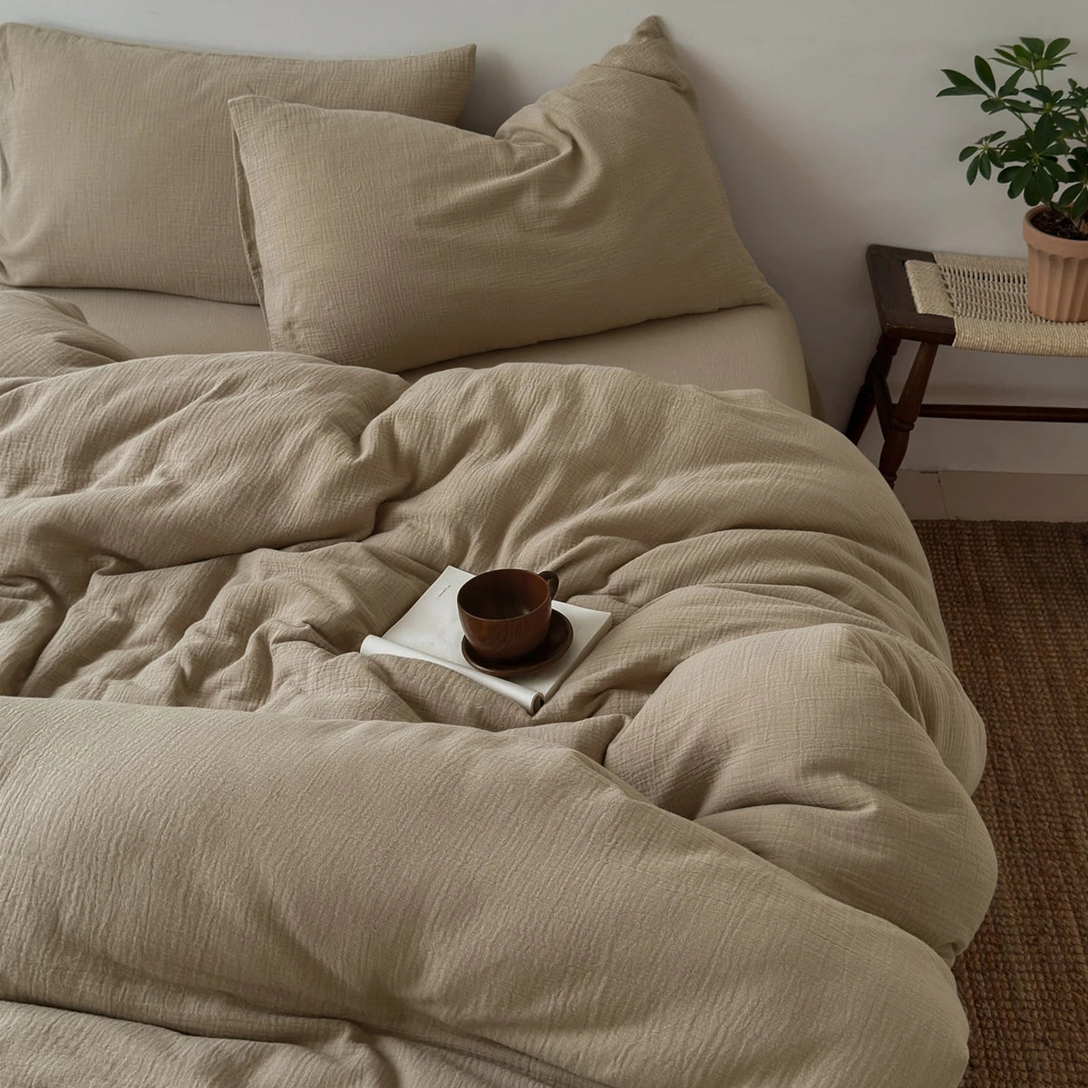 Beige, faltige Bettdecke mit passenden Kissen und Holzregal im Hintergrund.