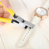 A hand is using silver leather hole punch pliers with a 2mm punch to pierce a white leather strap on a wooden surface.