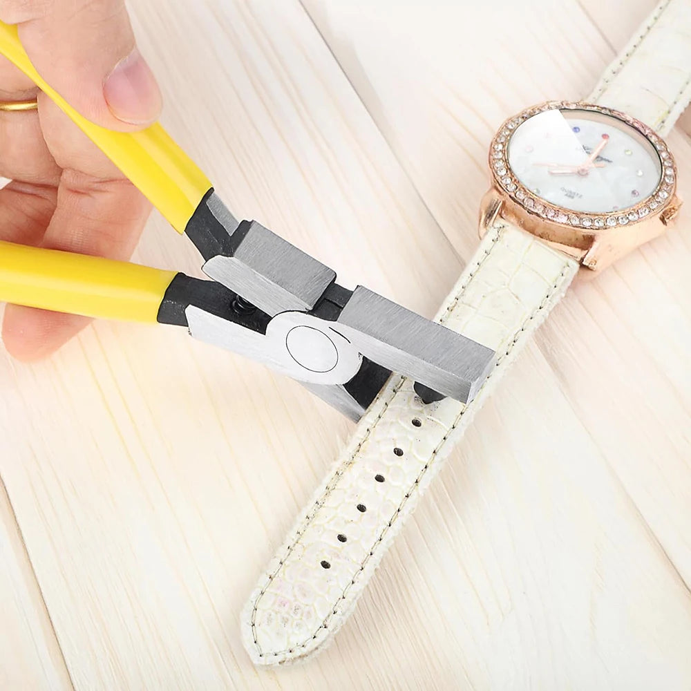 A hand is using silver leather hole punch pliers with a 2mm punch to pierce a white leather strap on a wooden surface.