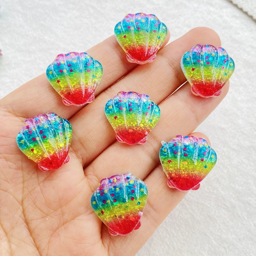 Hand holding colorful iridescent resin sea shell charms in various shades of blue, green, and red.