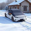 A white car with a black magnetic windshield cover is parked on a snowy driveway in front of a house.