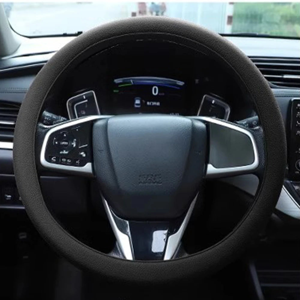 Close-up view of a black steering wheel with an anti-slip silicone cover and controls inside a car interior.