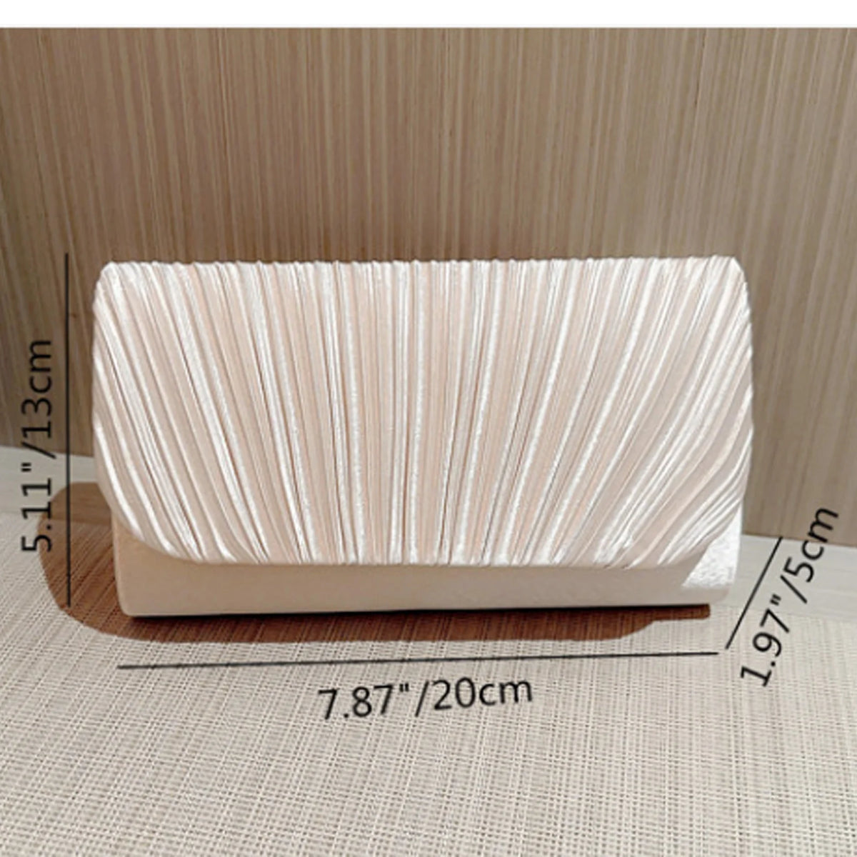 A rectangular clutch bag made of light pink patent leather with vertical pleats and a gold chain strap.