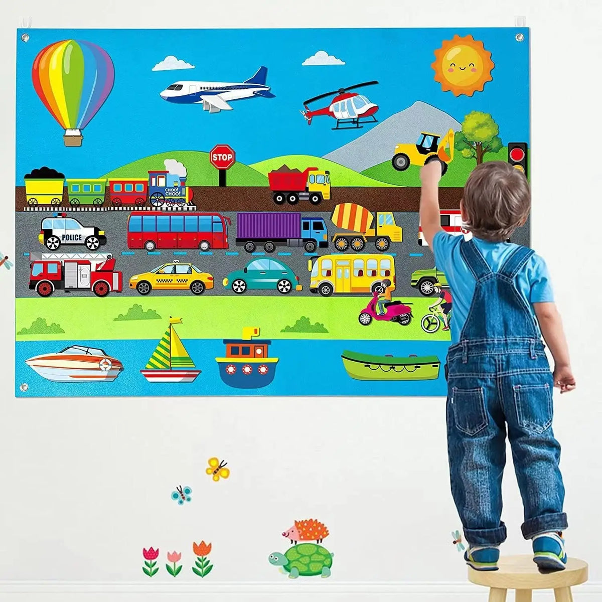 A child stands in front of a colorful felt board featuring various vehicles, animals, and a hot air balloon.