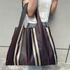 A person is holding a dark brown and beige striped foldable oxford cloth tote bag against a gray wall.