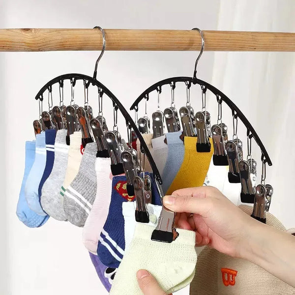 A hand hangs a collection of multi-clip hangers for pants, socks, and accessories from a wooden rod.