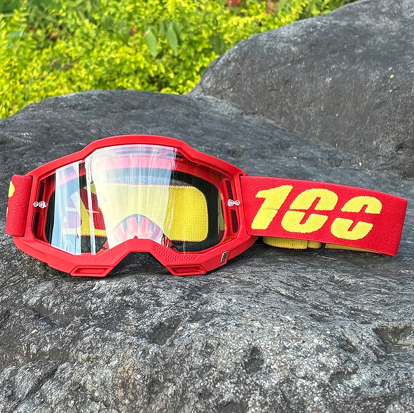 Red motocross goggles with yellow strap resting on a dark rock.