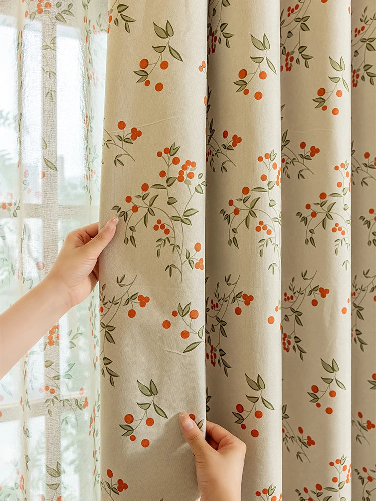 A beige blackout curtain panel with a green plant pattern is being held by a hand next to a window.
