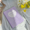 A purple composition notebook with a heart design is placed on a white cloth next to a pencil and some yellow flowers.