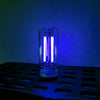 A clear glass LED night light with a warm filament glow is placed on a black tray against a blue background.