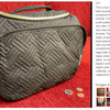 A dark quilted toiletry bag with a gold zipper and handle resting on a red fabric surface.