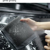 A hand is using a dark gray clay bar detailing towel to gently grind stubborn stains off a car surface.