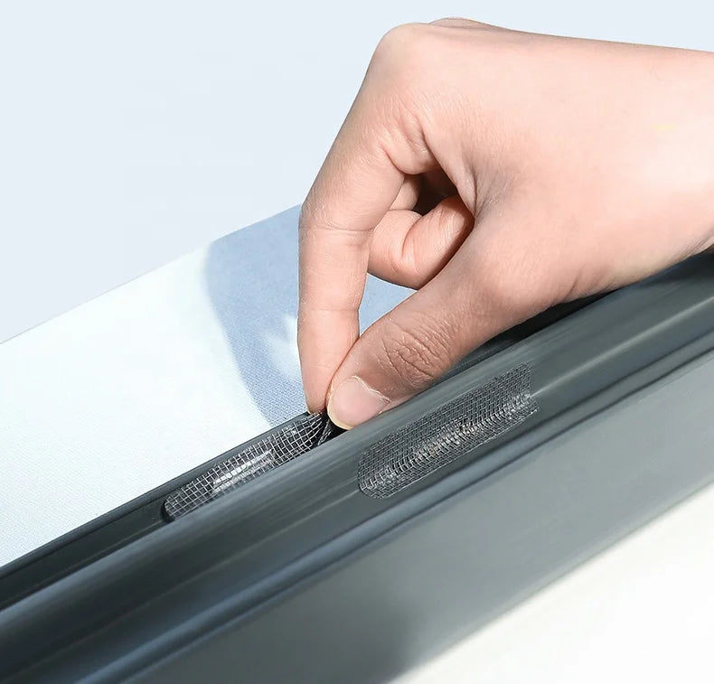A hand is applying a self-adhesive window screen repair patch to the edge of a window frame.