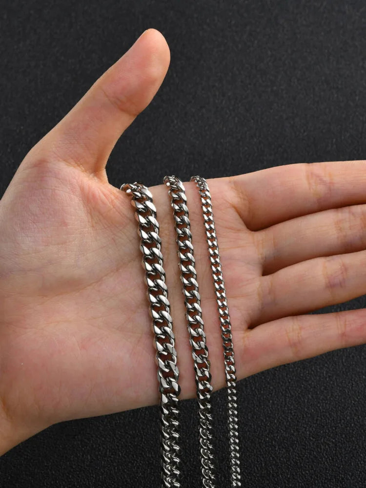A hand holds several strands of a stainless steel Cuban link chain necklace against a dark background.
