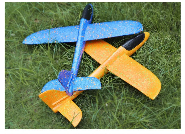 Two foam glider planes, one blue and one orange, resting on green grass.