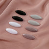 A set of eight oval scarf pins in black, white, and various shades of pink are displayed on a pink fabric.