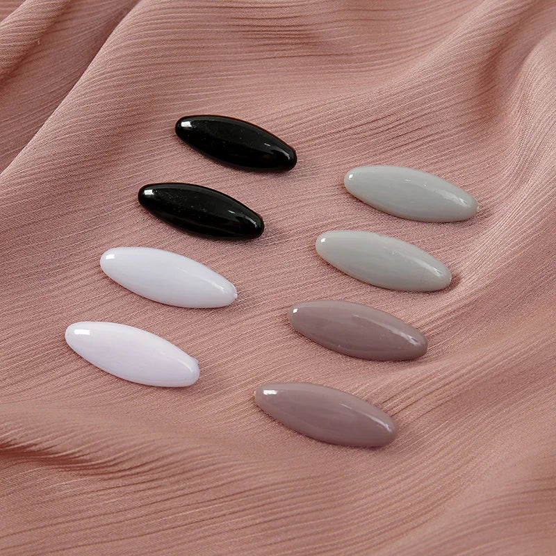 A set of eight oval scarf pins in black, white, and various shades of pink are displayed on a pink fabric.