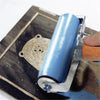 A close-up view of a blue rubber ink roller set being used for printmaking or stamping on a wooden surface.