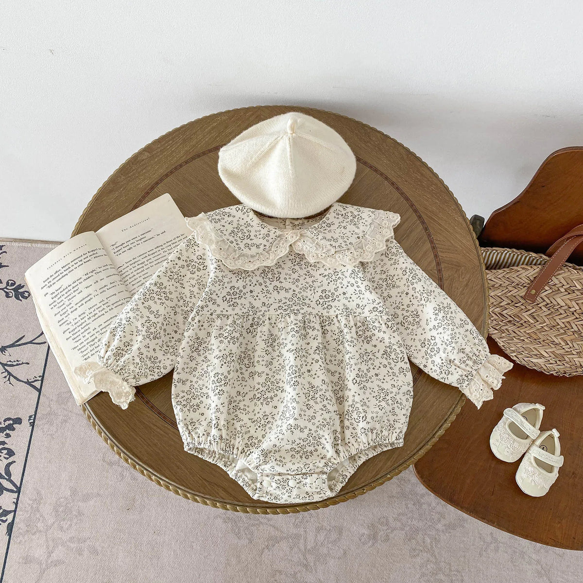 A cream floral lace cotton romper for a baby girl is displayed on a wooden tray.