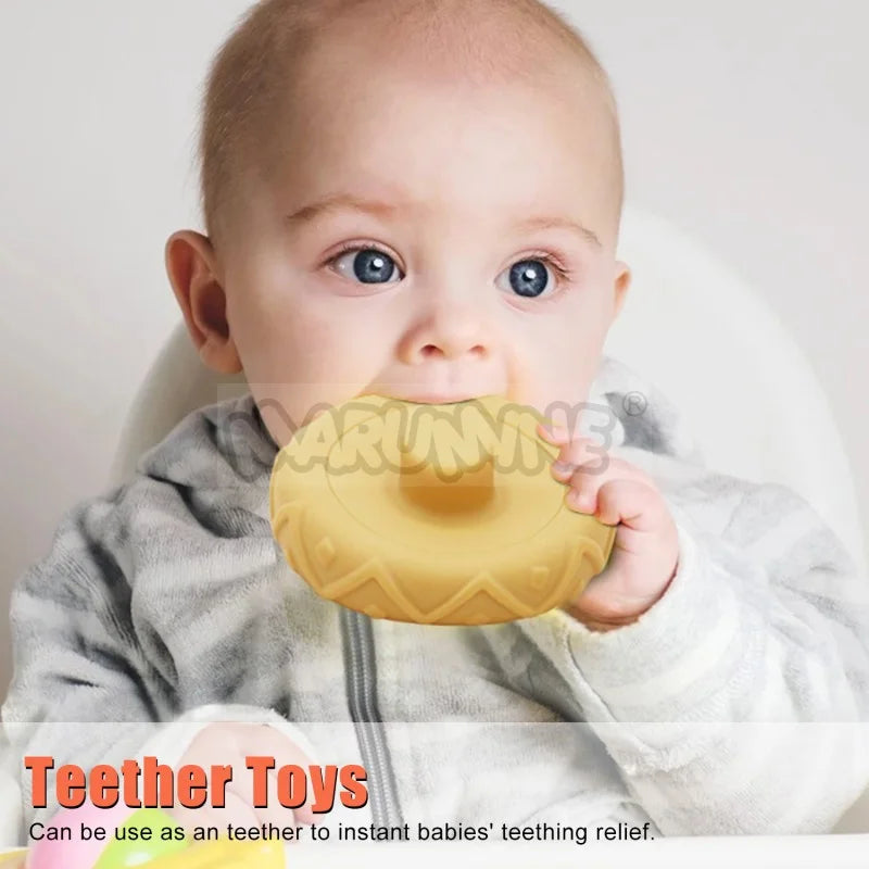 A baby is holding a yellow silicone stacking ring teether toy.