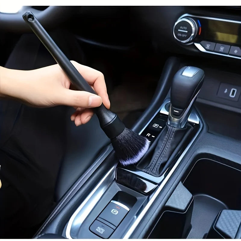 A hand is using a soft bristle interior detailing brush to clean the gear shift and console of a car.