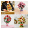 A pink and red cherry blossom bouquet displayed in a glass vase on a light pink surface.
