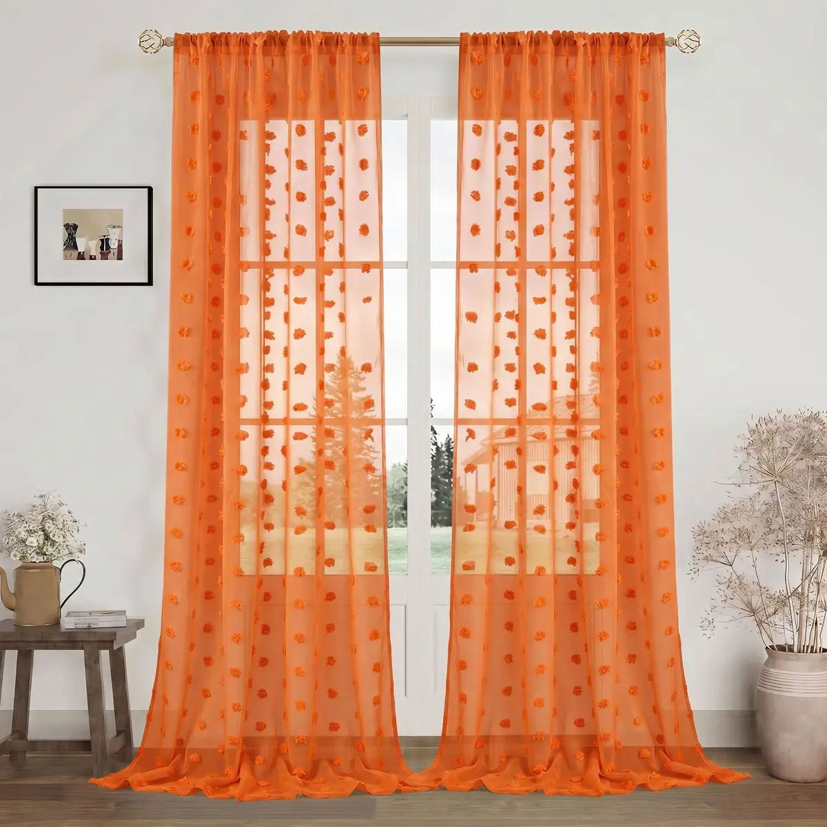 Orange sheer curtains with a floral pattern hanging in a glass door frame.