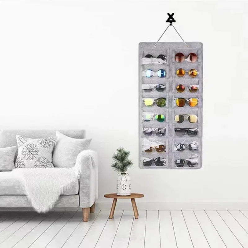 A grey felt eyewear organizer with sixteen slots is mounted on a white wall above a sofa.