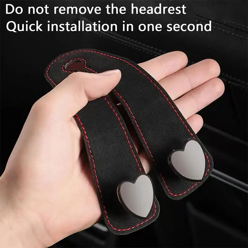 A hand holds a black car seat headrest hook with dual heart-shaped grips for quick installation.