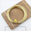 Gold anodized aluminum jewelry wire coiled on a wooden board with thin twine.