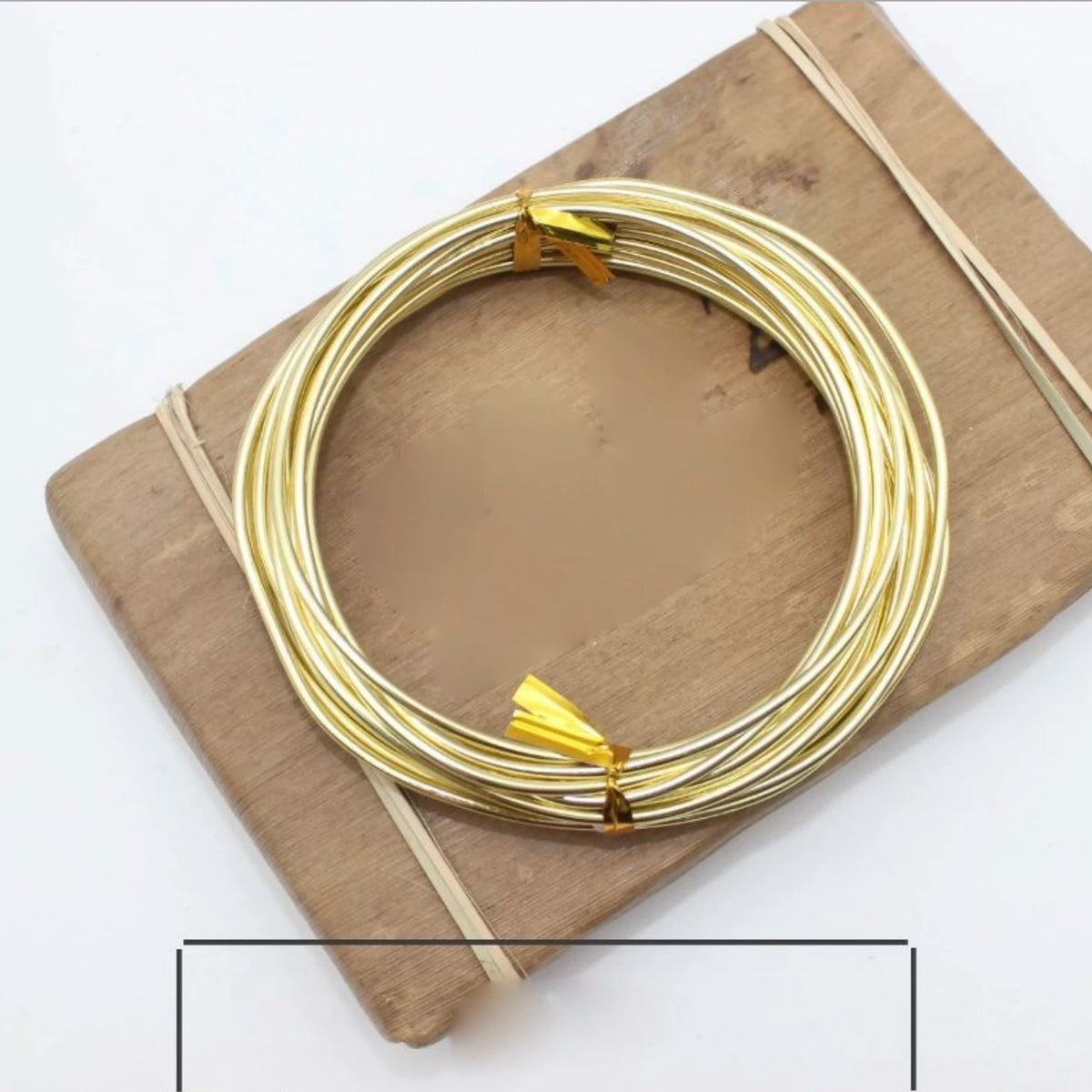 Gold anodized aluminum jewelry wire coiled on a wooden board with thin twine.