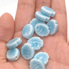 A hand holds a collection of light blue handcrafted ceramic fish beads for jewelry making