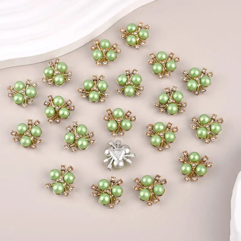 A collection of twenty pearlized resin flower beads in various shades of green and gold-toned metal, arranged on a light back