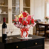 A vibrant bouquet of red and pink roses and cherry blossoms displayed in a white vase on a dark table.