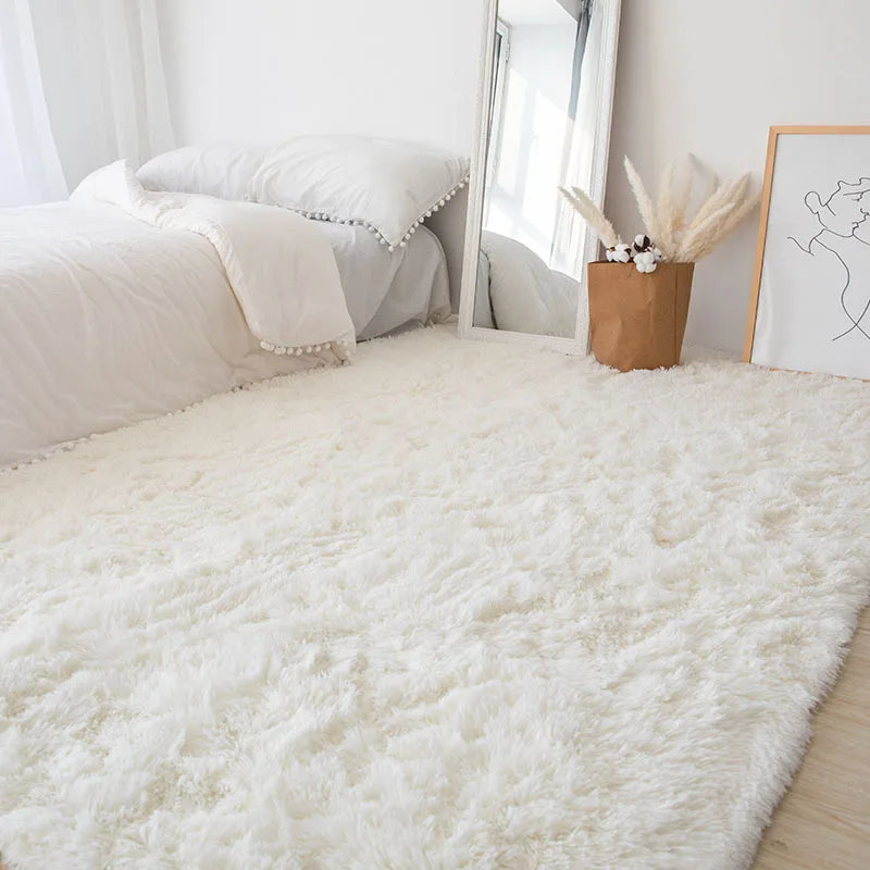 A fluffy white Nordic fur rug placed on a light wood floor next to a bed and a mirror.