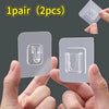 A pair of clear, double-sided adhesive wall hooks are shown being held by hands.