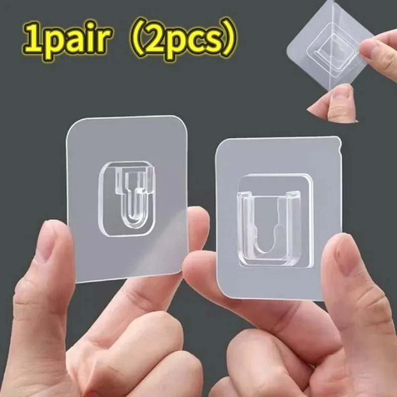 A pair of clear, double-sided adhesive wall hooks are shown being held by hands.