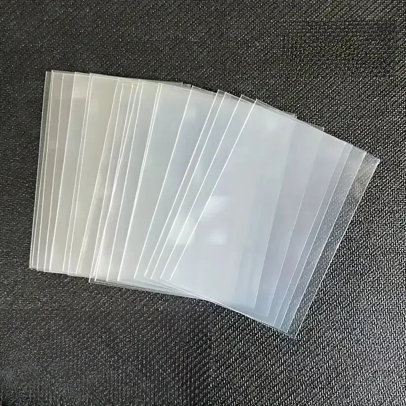 A fan of clear plastic card sleeves stacked diagonally on a dark surface.